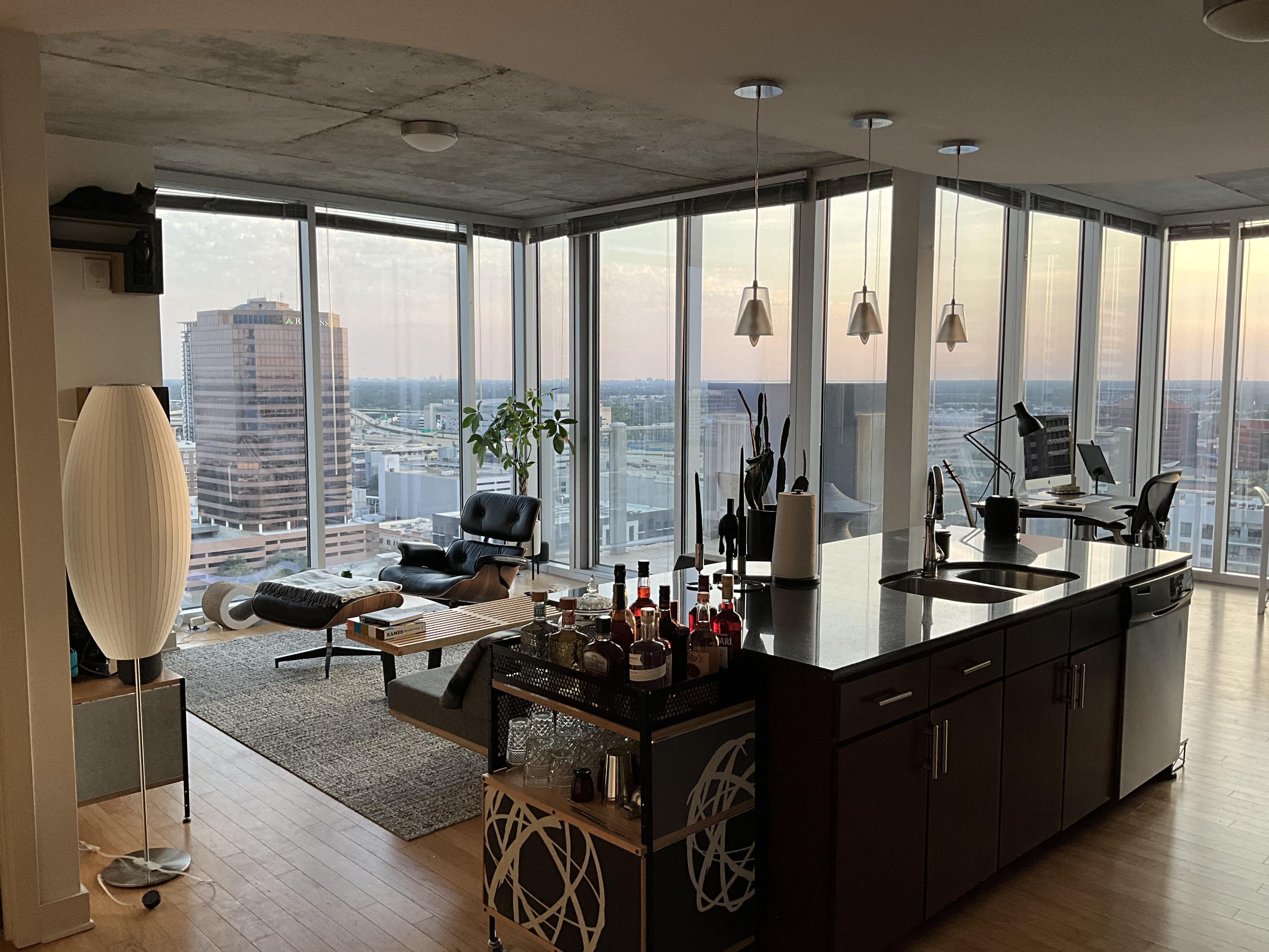 This luxurious living space boasts floor-to-ceiling windows that offer breathtaking views of the city. The unique design elements include a bookcase that doubles as a hidden door, a breaker box turned magnetic board, and a strategically placed cat figurine. The space is furnished with iconic pieces such as the Eames Lounge Chair and LC4, creating a modern and sophisticated atmosphere. The attention to detail and resourcefulness in design make this living space truly one-of-a-kind. /2023_04_04_12b3f6s/jdmgxolshrra1.jpg
