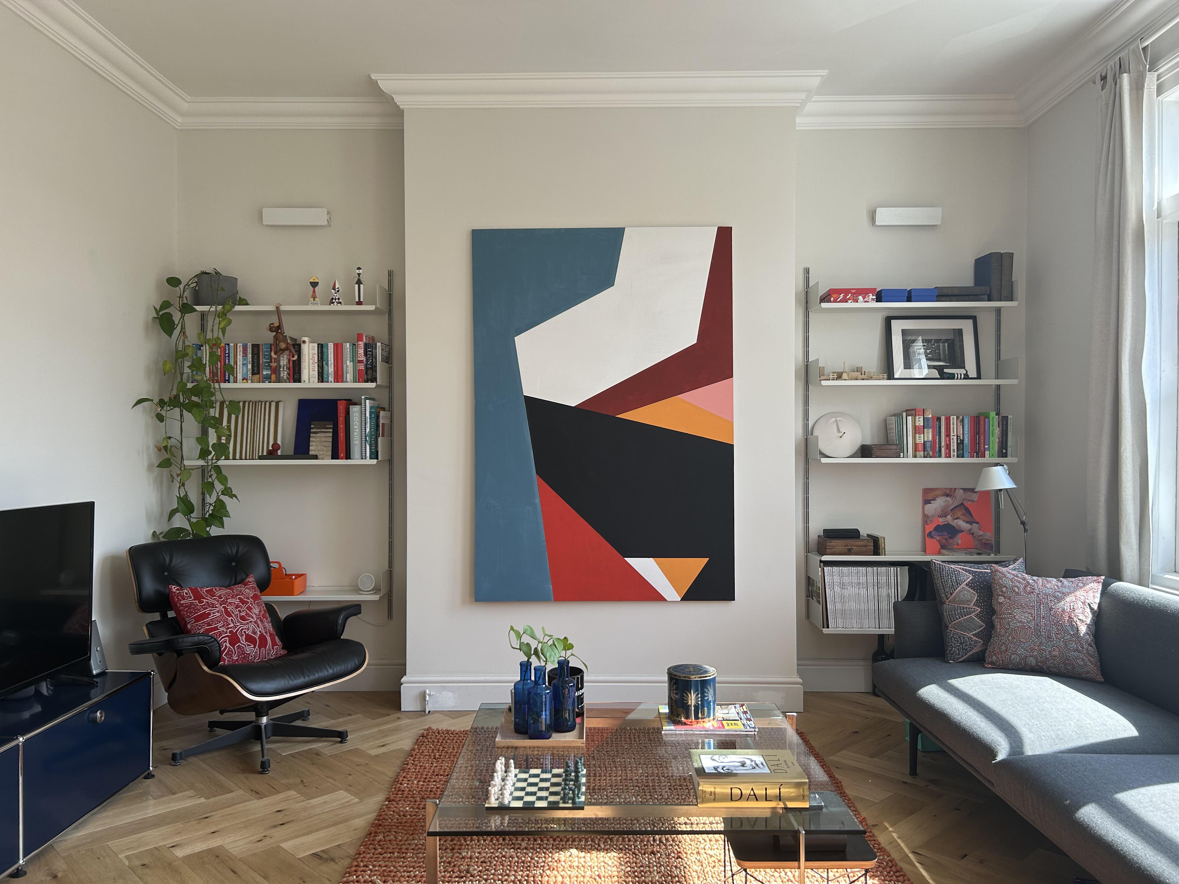 This London living space boasts a bold and eye-catching art piece that serves as the focal point of the room. The painting, self-made by the homeowner, features striking shapes and colors that tie the space together. The room also features modular design elements, including Vitsoe 606 shelves and a USM cabinet set that was upcycled into a TV stand, bedside tables, and a console table. The space is completed with a comfortable and stylish Outline couch by Muuto and a rug that matches the colors in the painting. Overall, this living space showcases a unique and personalized design that combines bold art with functional and modular furniture. /2023_04_09_12ggv1v/9dmzcbwsyvsa1.jpg