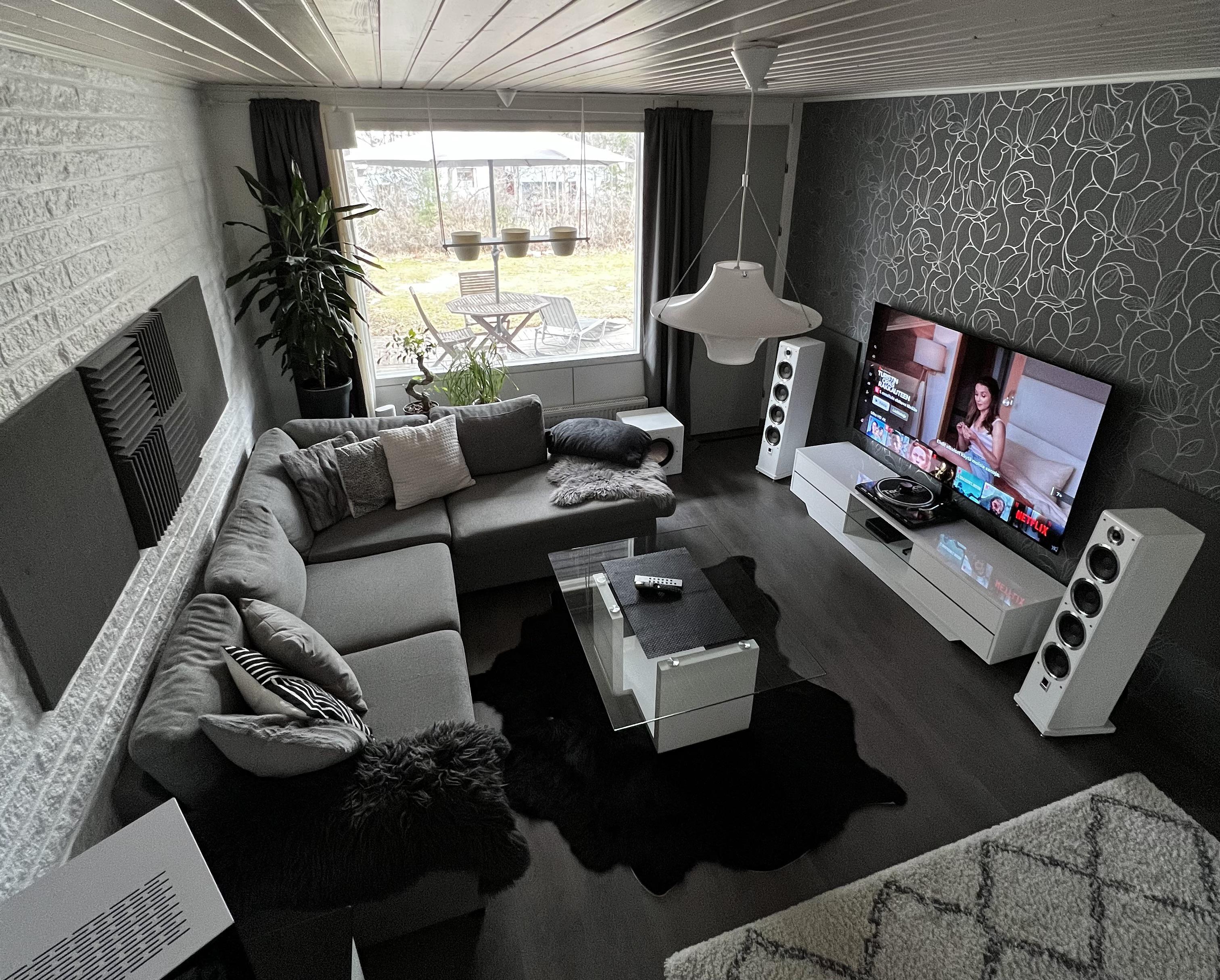 This Finnish living space showcases a stunning example of monochrome minimalism. The room features a slatted ceiling, gray doors, and black and white wallpaper. The furniture is a mix of textures and patterns, with a comfortable-looking couch and a sleek computer case. Acoustic panels on the walls and behind the couch add a functional element to the design. The room is accented with a few plants, including a ponytail palm and a bonsai tree, which thrive next to a water circulation heater. The overall effect is a calming and peaceful space that is both stylish and functional. /2023_04_23_12waqmv/axxo8kv5rova1.jpg